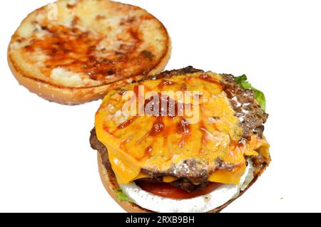 Ein saftiges, dickes, doppeltes Rinderpatty mit Käse, der mit Sauce bedeckt ist, knackigem Salat, frischen Tomaten, Zwiebeln und Gurken in einem großen Sesambrötchen, einem Rindfleisch Stockfoto