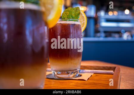 Kalter, mehrschichtiger Kaffeegetränk mit Zitronenscheibe und Minzblatt. Lemonada, Limonade oder Mineralwasser, Espresso, serviert auf Holztablett im Café. Selektiver Fokus, verschwommener Hintergrund Stockfoto