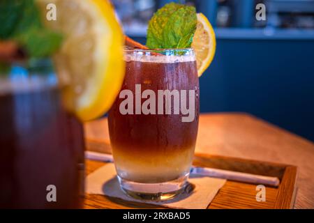 Kalter, mehrschichtiger Kaffeegetränk mit Zitronenscheibe und Minzblatt. Lemonada, Limonade oder Mineralwasser, Espresso, serviert auf Holztablett im Café. Selektiver Fokus, verschwommener Hintergrund Stockfoto