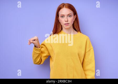 Innenaufnahme einer jungen ernsthaften Ingwerdame in lässiger Kleidung, die die Hand beim Erlernen der Gebärdensprache hochhält, isoliert über blauem Hintergrund. Handgriff Stockfoto