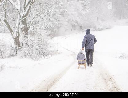 Ein Vater, der sein Kind am schneebedeckten Wintertag rodeln lässt. Familienurlaub im Winter. Stockfoto