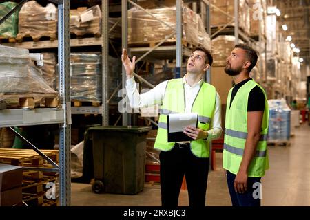 Leute Lagerarbeiter sprechen, Lagerindustrie und Logistikkonzept. Zwei junge Arbeiter in Uniform diskutieren miteinander. Konzept der guten Führungsrolle Stockfoto