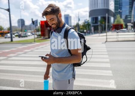 Lächelnder Mann mit Telefon und einer Flasche Wasser auf Wolkenkratzern im Hintergrund nach dem Training Stockfoto