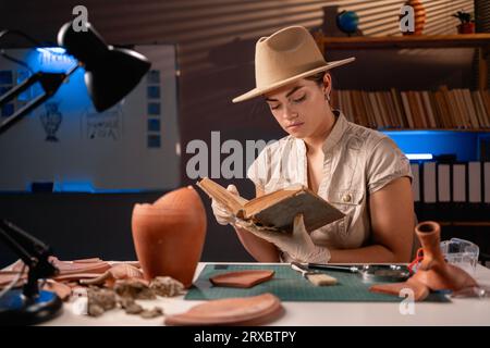 Archäologe, der spät abends im Büro arbeitet und ein altes Buch über Archäologie liest Stockfoto