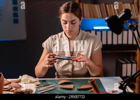 Junger Archäologe, der Keramikstücke von Amphoren studiert und nachts im Büro arbeitet, um alte Artefakte zu fotografieren. Stockfoto