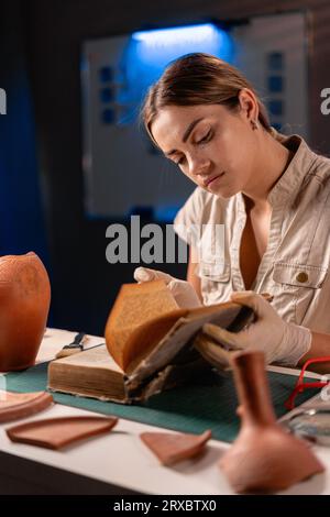 Archäologe, der spät abends im Büro arbeitet, Buch liest und Keramikvase studiert Stockfoto