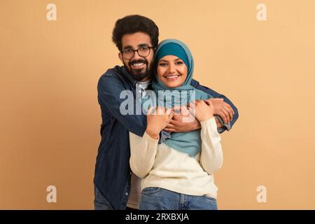 Porträt Eines Jungen Lächelnden Muslimischen Paares, Das Sich Über Beiges Hintergrund Umgibt Stockfoto