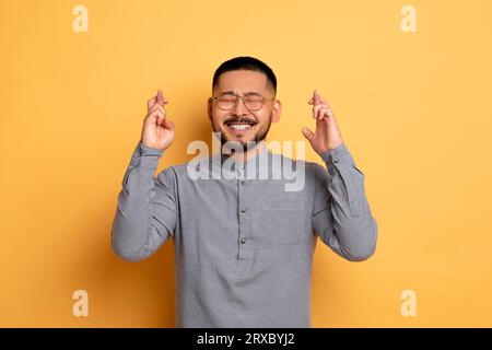 Wünschen. Porträt Eines Fröhlichen Jungen Asiaten, Der Die Daumen Drückt Stockfoto
