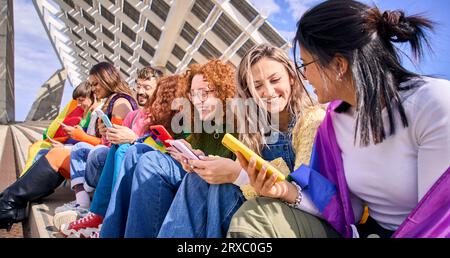 Seitenansicht große, multirassische Gruppen junger Freunde, die Mobiltelefone im Freien benutzen. LGBT vielfältige Community. Stockfoto