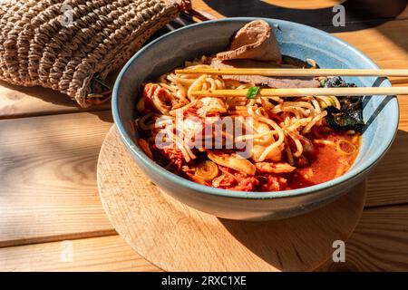 Auf dem rustikalen Holztisch steht eine Schüssel traditioneller Ramen-Suppe, begleitet von Stäbchen. Stockfoto