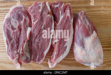 Eine Lammschulter wird in vier Stücke geschnitten und in weißes Papier auf einem Holztisch gewickelt. Stockfoto