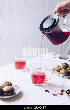Heißer Hibiskus-Tee aus der Teekanne aus Glas in eine Glasschale gießen Stockfoto