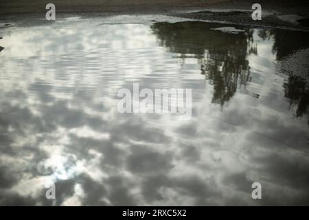 Wolken werden in Pfützen reflektiert. Bewölktes Wetter draußen. Riesige Pfütze auf Asphalt. Wasseroberfläche. Stockfoto