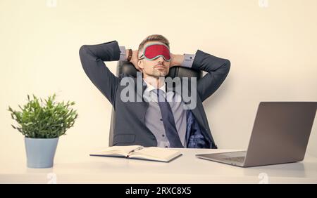 Müde Unternehmer entspannen in Schlafmaske am Arbeitsplatz. Stockfoto