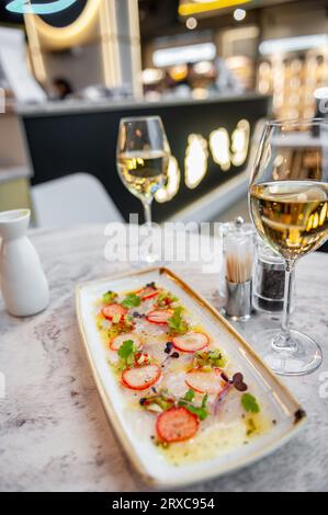 Wolfsbarsch-Ceviche mit Erdbeeren, Kiwi und Mangosalsa auf einem Marmortisch in einem Restaurant und einem Glas Weißwein Stockfoto