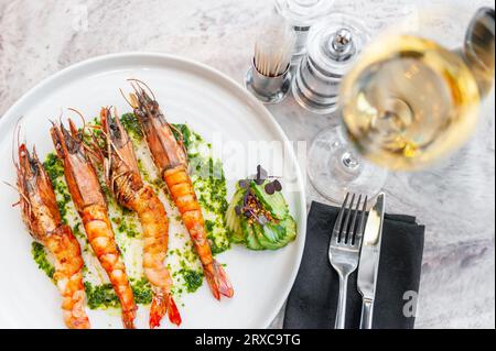 Langusten mit Spinatsoße auf einem weißen Teller mit einem Glas Weißwein Stockfoto