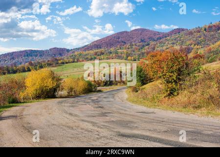 Alte, rissige Landstraße durch bergige Landschaft. Bunte Naturkulisse in der Herbstsaison an einem sonnigen Vorabend Stockfoto