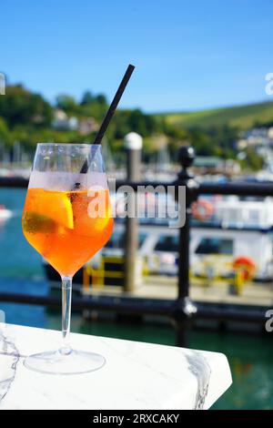 Erfrischender Alkohol aperol Spritz, Sommercocktail. River Dart und Dartmouth Hafen im Hintergrund Stockfoto