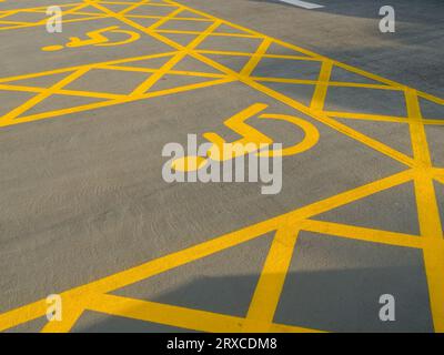 Zwei frisch lackierte Behindertenparkplätze in gelber Farbe mit Kreuzschraffur und Behindertensymbol auf dem Parkplatz, England, Großbritannien Stockfoto