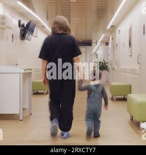 Das Baby hält sich fest am Arm seiner Mutter, während sie durch die Kinderkrankenabteilung gehen. Kind im Alter von zwei Jahren (zweijähriger Junge) Stockfoto