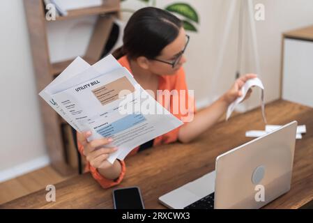 Die Frau füllt das Steuerformular aus und hält den aktuellen Spesenbeleg in Händen, während sie zu Hause am Arbeitsplatz sitzt Stockfoto