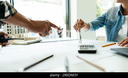 Zwei Konstrukteure arbeiten und verwenden den Geometriekompass, um ein Konstruktionsprojekt auf dem Blueprint zu zeichnen. Stockfoto