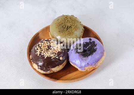 Köstliche süße Donuts mit verschiedenen Aromen auf Holzteller serviert. Isoliertes Bild auf weißem Hintergrund Stockfoto