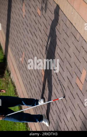 Eine gesichtslose blinde Frau läuft mit einem Stock die Straße entlang. Stockfoto