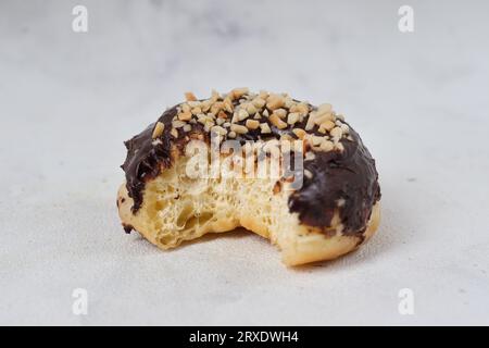 Reste-Konzept von köstlichem süßen Schokoladen-glasierten Donut mit Cashewnüssen, die auf einem Tisch serviert wurden. Isoliertes Bild auf weißem Hintergrund Stockfoto