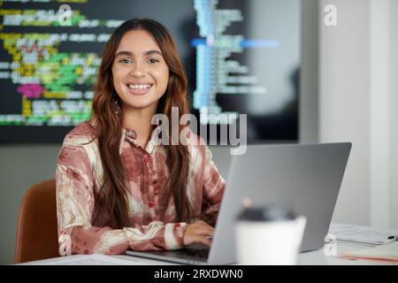 Porträt eines jungen, freudigen Softwareentwicklers, der im modernen Büro am Laptop arbeitet Stockfoto