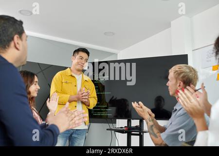 Das Team klatscht nach seiner Präsentation des erfolgreichen Projekts zum Sprecher in einem Geschäftstreffen Stockfoto