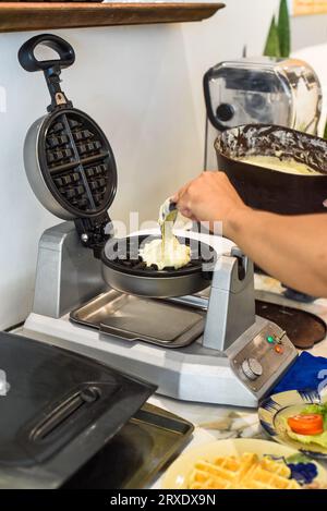 Der Koch gibt den Teig für süße Waffeln mit einem Löffel in das Waffeleisen Stockfoto