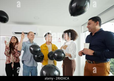 Fröhliches Team wirft Ballons, wenn es den Start eines erfolgreichen Projekts im Büro feiert Stockfoto