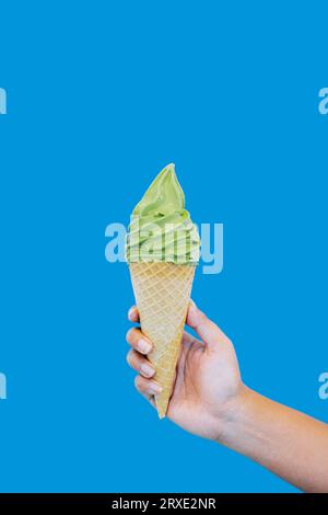 Matcha Ice Cream Cone wird von Hand auf isoliertem blauem Hintergrund gehalten Stockfoto