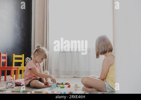 Kinder spielen mit bunten Holzspielzeugblöcken und Ziegeln. Kinder sitzen auf dem Boden im sonnigen weißen Schlafzimmer oder Kindergarten, Kindertagesstätte Spielzimmer Stockfoto