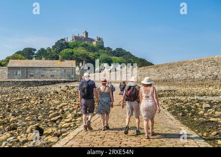 14. Juni 2023: Marazion, Cornwall, Großbritannien - Paare gehen Hand in Hand auf dem Damm zum St. Michael's Mount, an einem wunderschönen Sommertag. Stockfoto