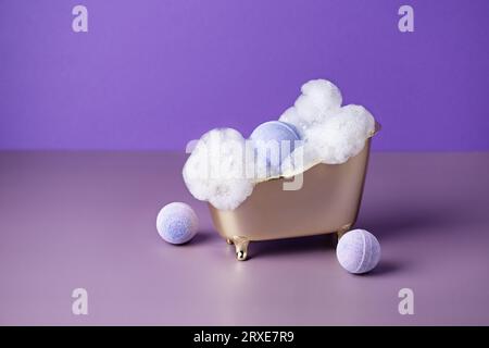 Salzbadbombe in einer Badewanne mit Seifenlauge auf violettem Hintergrund. Kreative Idee von Badebomben für Körperpflege-Beauty-Spa-Behandlungen. Stockfoto