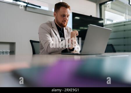 Schwacher Blick auf einen müden Geschäftsmann im formellen Anzug, der unter Handgelenkschmerzen leidet, der am Laptop arbeitet, der am Arbeitsplatz in einem modernen Büro sitzt. Erschöpft traurig Stockfoto