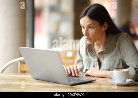 Staunte Frau, die überraschende Inhalte auf einem Laptop auf einer Restaurantterrasse sah Stockfoto