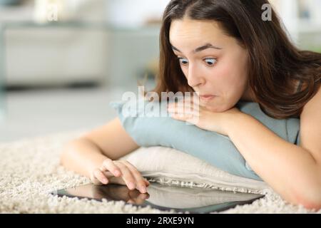 Perplexte Frau, die ein Tablet zu Hause auf dem Boden anlegt Stockfoto