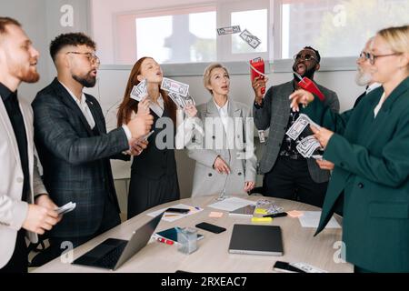 Ein fröhliches Business-Team aus Mitarbeitern im gemischten Alter, die Spaß haben, springen und sich über den Sieg freuen. Glücklicher afrikanisch-amerikanischer männlicher Boss, der Geld verwendet Stockfoto