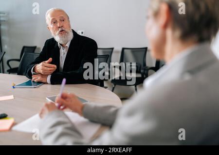 Selektiver Fokus eines erfahrenen männlichen Teamleiters im Erwachsenenalter, der mit Kollegen unterschiedlichen Alters spricht, um sich zu treffen und die Projektstrategie mit dem Team zu besprechen. Stockfoto