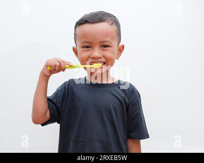 Kleiner asiatischer Junge, der seine Zähne putzt, während er auf weißem Hintergrund mit Kopierraum lächelt. Kinderzahngesundheitskonzept Stockfoto