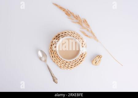 Kaffeetasse auf einer Korbbahn, Löffel und Pampasgras auf weißem Hintergrund. Stillleben. Draufsicht, flach. Stockfoto