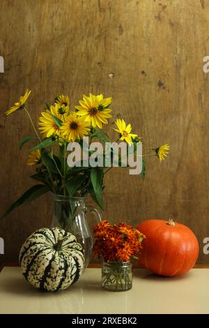 Ein Stillleben mit wilden Sonnenblumen in einer Vase und bunten Kürbissen Stockfoto