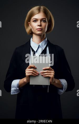 Trendige blonde Geschäftsfrau mit Notizblock auf schwarzem Hintergrund Stockfoto