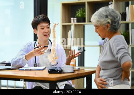 Orthopäde in weißer medizinischer Laborkittel zur Problemstellung am Wirbelsäulenmodell bei reiferen Patientinnen Stockfoto