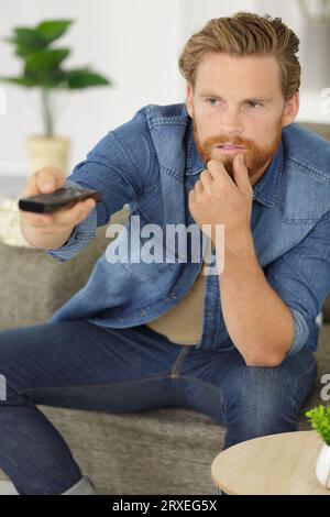 Junger Mann wechselt die Sender auf der Fernbedienung Stockfoto