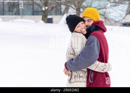 Junge Paare, die sich im Winter im Park umarmen, Mann und Frau, die sich verliebt haben. Glückliches Paar, das sich im Winter im Freien umarmt Stockfoto