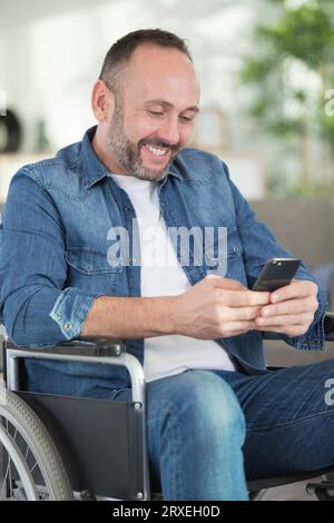 Junger Mann im Rollstuhl, glücklich mit dem Handy Stockfoto